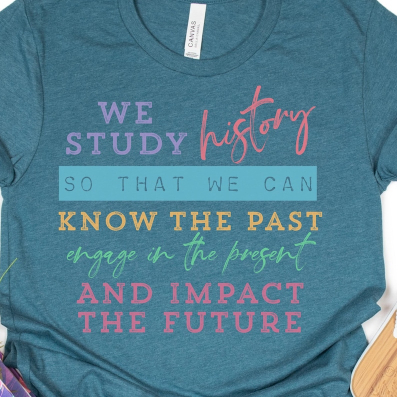 May include: Teal blue t-shirt with a quote in colorful text that reads "We study history so that we can know the past engage in the present and impact the future."