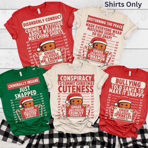 May include: A collection of Christmas-themed t-shirts in red, green, and cream colors. Each shirt features a gingerbread man design with a Santa hat and candy cane accents, along with humorous text. The shirts are displayed on a black and white checkered surface.