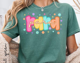 May include: A light green t-shirt with the word "Para" in colorful, bubble letters. The word is surrounded by small flowers and stars. The shirt has short sleeves and a crew neck.