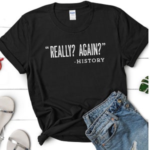 May include: Black t-shirt with white text that reads "Really? Again? - History"