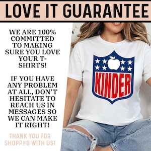 May include: White t-shirt with a red, white, and blue shield design. The shield has an apple and stars and the word "KINDER" in red letters.