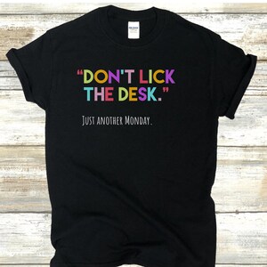 K&ouml;nnte beinhalten: Schwarzes T-Shirt mit dem Text "DON'T LICK THE DESK." in Regenbogenfarben und dem Text "JUST ANOTHER MONDAY." in Wei&szlig; darunter.