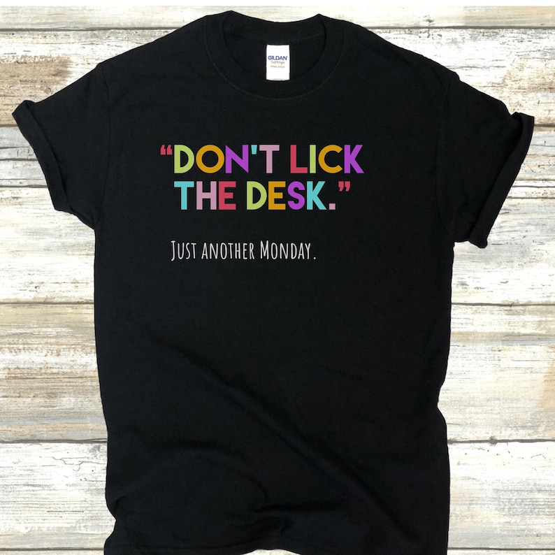 K&ouml;nnte beinhalten: Schwarzes T-Shirt mit dem Text "DON'T LICK THE DESK." in Regenbogenfarben und dem Text "JUST ANOTHER MONDAY." in Wei&szlig; darunter.