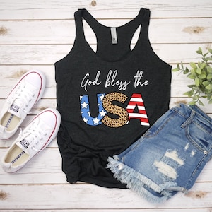 May include: A black tank top with the text "God bless the USA" in white. The letters are decorated with red, white, and blue stars and stripes, and a leopard print.
