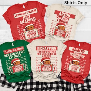 May include: A collection of Christmas-themed t-shirts in red, green, and cream colors. Each shirt features a gingerbread man design with humorous text like "Criminally Insane" and "Arson One Hot Cookie". The shirts have a jailhouse lineup graphic.