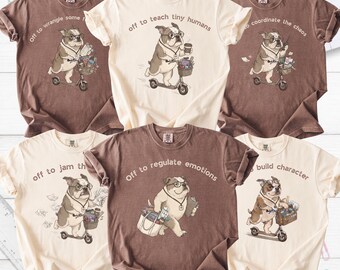 May include: Six short-sleeved crew neck t-shirts in brown and cream colors. Each shirt features a graphic of a bulldog wearing glasses and carrying school supplies, with text including phrases like off to teach tiny humans and off to regulate emotions.