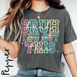 May include: A gray t-shirt with the text "BRUH YOU GOT THIS" in rainbow colors. The text is in a bold, blocky font.