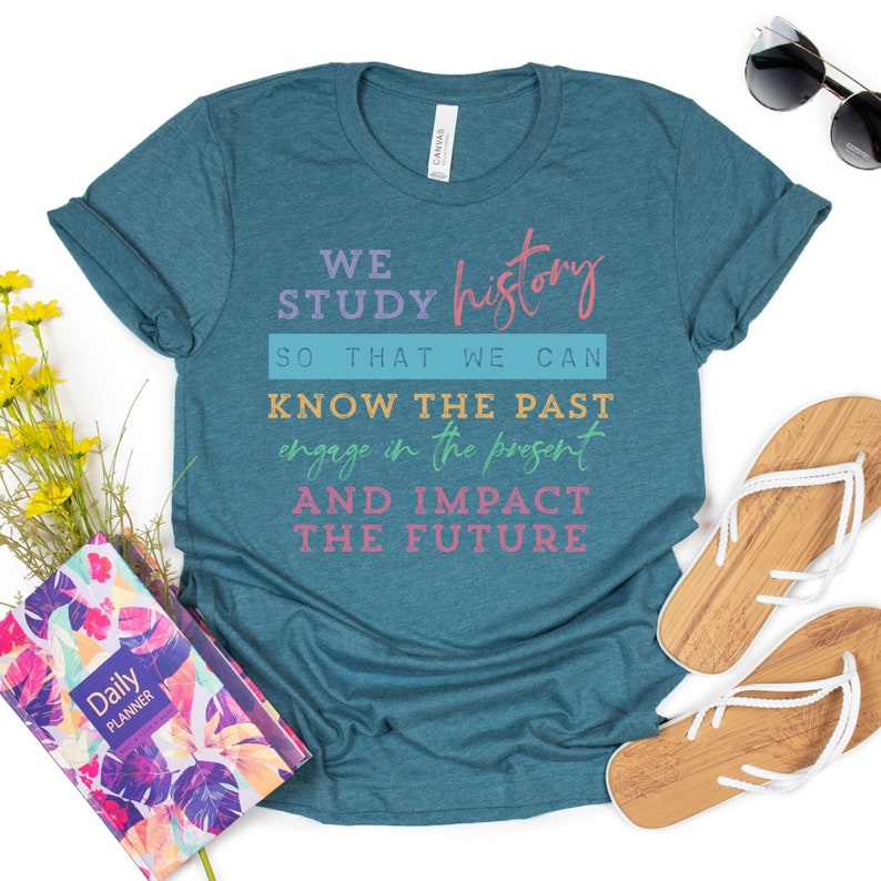 May include: Teal blue t-shirt with the text "WE STUDY history SO THAT WE CAN KNOW THE PAST engage in the present AND IMPACT THE FUTURE" in pink, orange, and blue lettering.