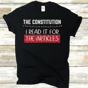 May include: Black t-shirt with the text "THE CONSTITUTION I READ IT FOR THE ARTICLES" in white. The text is surrounded by gold stars and a red rectangle with white stars.