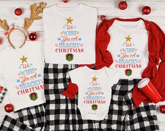 May include: White t-shirts and a baby onesie with the text "We Wish You A Beachy Christmas" in a Christmas tree design. The shirts are paired with black and white plaid pajama pants. Red accents include a cardigan, a cup, and ornaments.