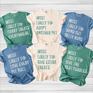 May include: Six short-sleeved crew neck t-shirts in cream, blue, and green. Each shirt features a distressed white graphic with the text "Most Likely To" followed by phrases like "Carry Treats Everywhere," "Adopt Another Pet," "Hand Out Belly Rubs," "Love Every Pit Bull," "Give Extra Treats," and "Give The Best Cuddles."