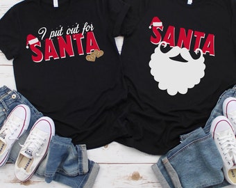 May include: Two black t-shirts with Christmas themed designs. One shirt says "I put out for Santa" with a Santa hat and two gingerbread cookies. The other shirt has a white Santa beard and hat.