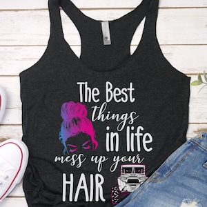 May include: A black tank top with the text "The Best things in life mess up your HAIR" in white. A graphic of a woman with a messy bun and a side-by-side vehicle is printed on the shirt.