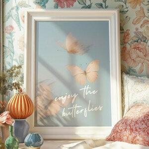 Op de afbeelding: Een witte ingelijste print met een lichtblauwe achtergrond waarop drie vlinders te zien zijn en de tekst "enjoy the butterflies".