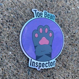 May include: A purple and silver holographic sticker with a paw print and the text "Toe Bean Inspector".