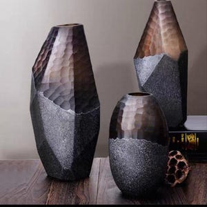 May include: Three decorative vases with textured surfaces. The vases have a two-tone design, with a dark brown upper section and a gray lower section. The vases vary in shape and size, with one tall and angular, another oval, and a third tall and rounded.