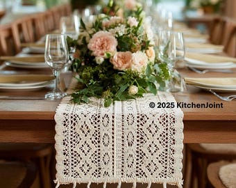 Può includere: Runner da tavolo in pizzo color crema con motivo geometrico e frange con nappe. È posto su un tavolo di legno apparecchiato per un evento formale, con composizioni floreali e bicchieri. Il testo "© 2025 KitchenJoint" è visibile.
