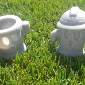 May include: Two gray 3D printed figurines with a hole in the middle. The figurine on the left has a rounded top and the figurine on the right has a flat top with a rounded brim.