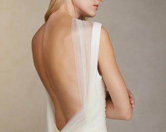 May include: A white sleeveless wedding dress with a tulle overlay that drapes over the back and ties at the waist.