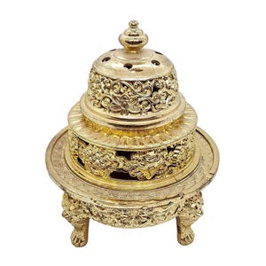 Puede incluir: Quemador de incienso dorado ornamentado con intrincados grabados florales y de dragones. El quemador tiene un diseño escalonado con una tapa en forma de cúpula y se apoya en tres patas con garras. Una pieza decorativa.