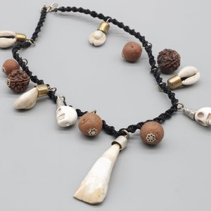 May include: A black cord necklace with various charms, including white seashells, brown beads, and silver skull pendants.