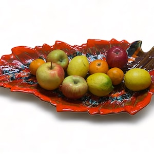 Peut inclure: Un bol à fruits en céramique rouge et marron en forme de feuille, rempli de pommes, de citrons et d'oranges.