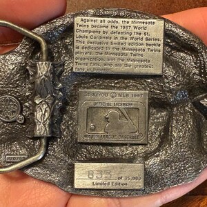 May include: A detailed, silver-toned metal belt buckle commemorating the Minnesota Twins' 1987 World Series victory. The buckle features text detailing the team's achievement, the MLB logo, and the limited edition number 833 of 25,000.