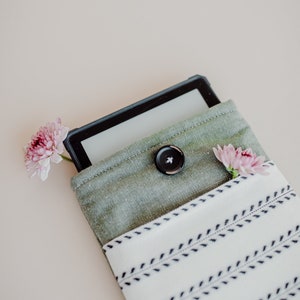 May include: A black e-reader in a green fabric case with a white and black striped fabric lining. The case has a button closure and is decorated with two pink flowers.