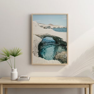 May include: A framed photograph of a natural rock archway over a turquoise blue ocean cove. The archway is made of white rock and the water is clear and calm.