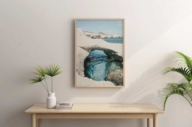 May include: A framed photograph of a natural rock archway over a turquoise blue ocean cove. The archway is made of white rock and the water is clear and calm.