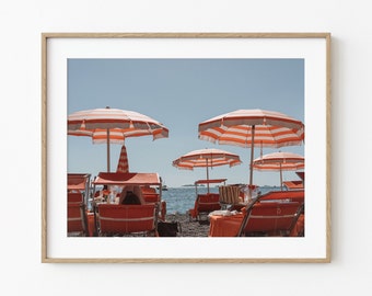 May include: A beach scene with red and white striped beach umbrellas and orange lounge chairs. The chairs are facing the ocean, and there are people sitting in some of them.