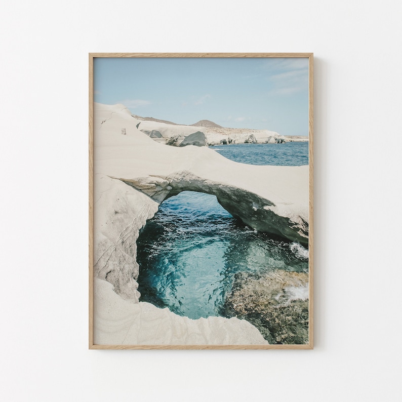 May include: A photograph of a natural rock archway on a white sand beach with turquoise blue water. The archway frames a view of the ocean.