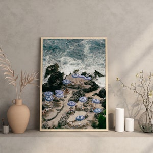 May include: A framed photograph of a rocky coastline with blue and white striped umbrellas and chairs. The water is crashing against the rocks and there are people sitting under the umbrellas.