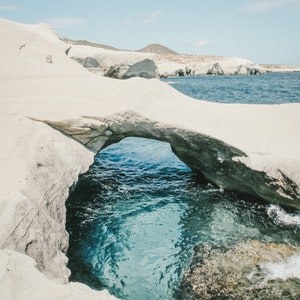 May include: A white rock formation with a natural archway overlooking a turquoise blue ocean cove.