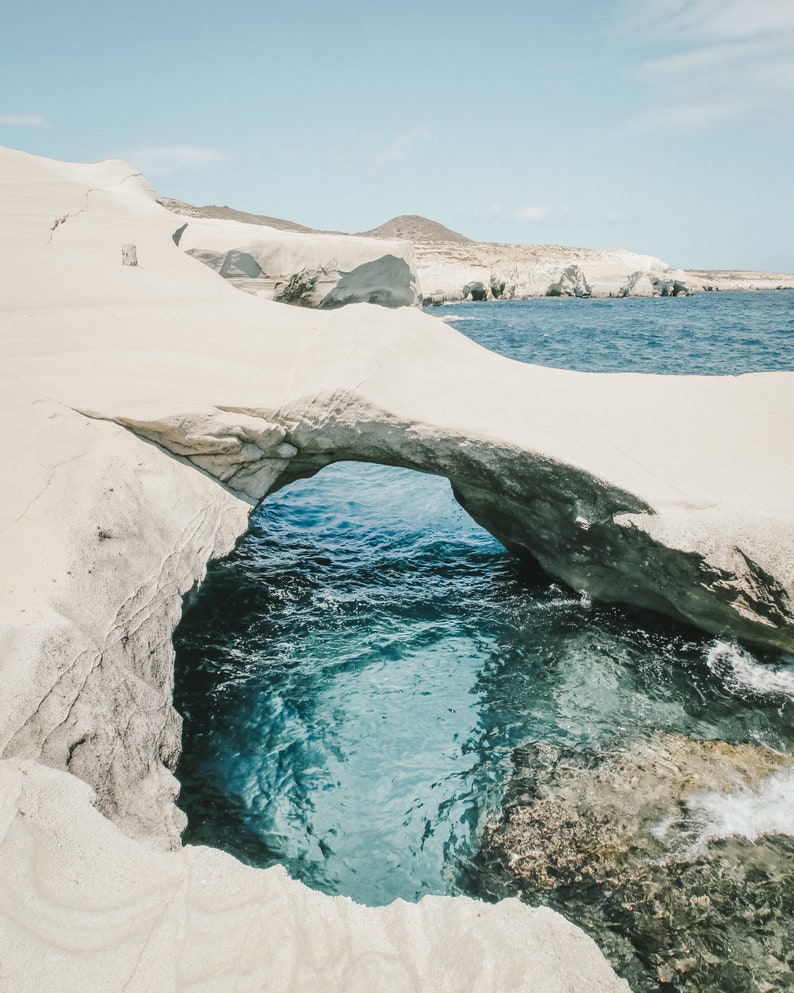 May include: A white rock formation with a natural archway overlooking a turquoise blue ocean cove.