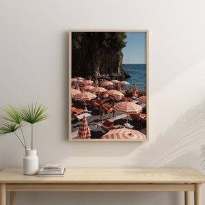 May include: A framed photograph of a beach scene with red and white striped umbrellas, people, and a rocky cliff in the background.