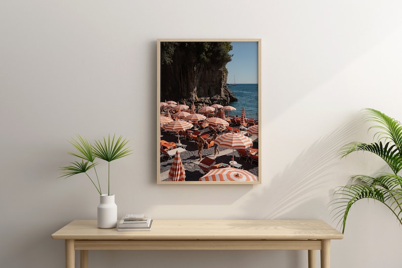 May include: A framed photograph of a beach scene with red and white striped umbrellas, people, and a rocky cliff in the background.