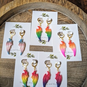 May include: Four pairs of rainbow gradient dragon wing earrings on white cards with the text "Stag and Bran" on each card.
