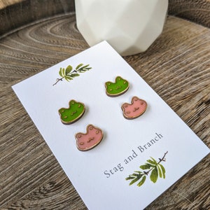 May include: Four wooden cat-shaped earrings, two green and two pink, displayed on a white card with the text "Stag and Branch".