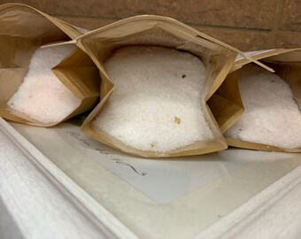 May include: Three brown paper bags filled with white bath salts. The bags are open and the salts are spilling out.