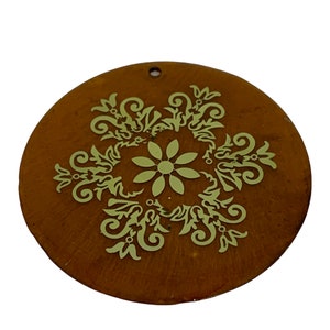 May include: A round, brown ornament with a gold-colored, intricate floral design. The ornament has a small hole at the top for hanging.