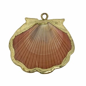 May include: A gold-toned pendant featuring a detailed seashell design with a pink and white interior. The pendant has a loop at the top for attaching to a chain.