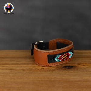 Può includere: Un braccialetto in pelle marrone con un design di perline colorate. Il braccialetto ha una chiusura a fibbia.