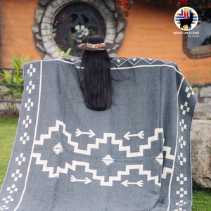 May include: A gray and white woven blanket with a geometric pattern featuring arrows. The blanket is folded and draped over a person's shoulders.