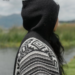 Pode incluir: Poncho preto e branco com capuz e um padr&atilde;o geom&eacute;trico. O poncho &eacute; feito de um tecido macio e tricotado.