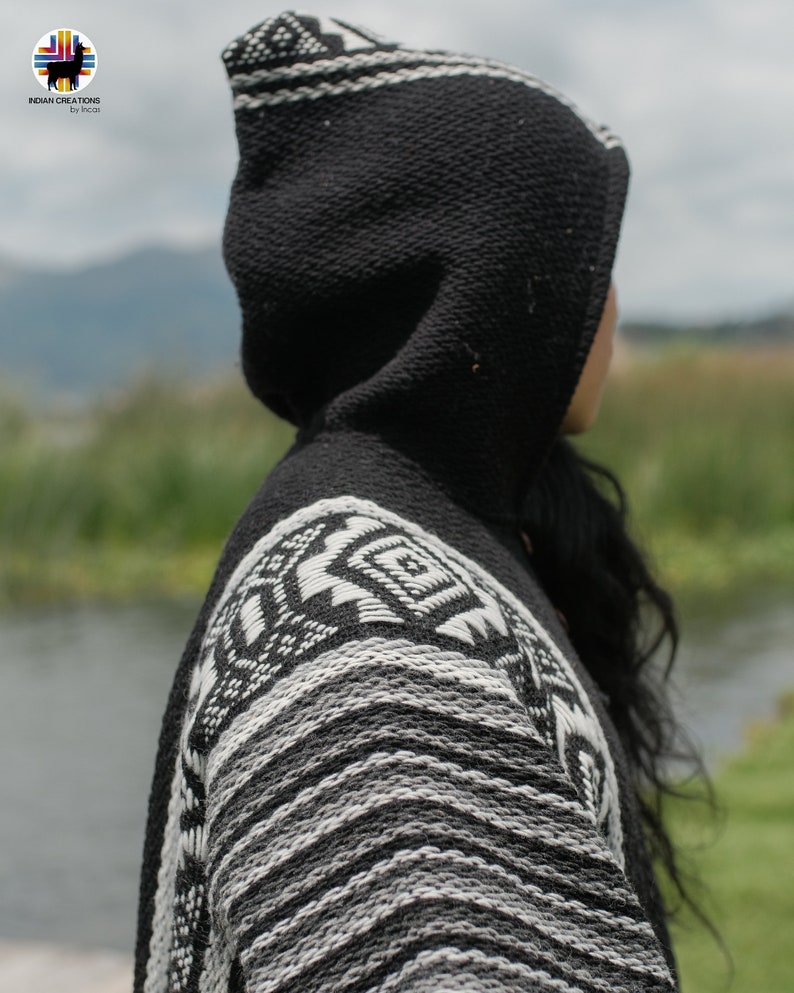 Pode incluir: Poncho preto e branco com capuz e um padr&atilde;o geom&eacute;trico. O poncho &eacute; feito de um tecido macio e tricotado.