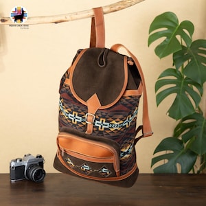 May include: A brown backpack with a flap closure and a front pocket. The backpack features a patterned fabric with geometric designs in shades of brown, orange, yellow, and blue. It has leather straps and accents. The backpack is hanging from a branch.