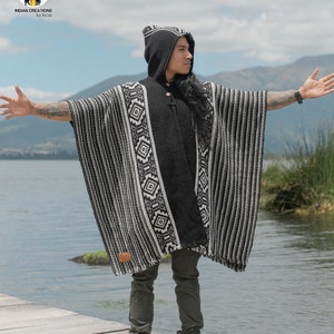 Pode incluir: Um poncho com capuz listrado preto e branco com um padr&atilde;o geom&eacute;trico. O poncho &eacute; feito de l&atilde; de alpaca e tem uma bainha de franjas. O modelo est&aacute; usando o poncho com uma cal&ccedil;a verde escura e botas marrons.
