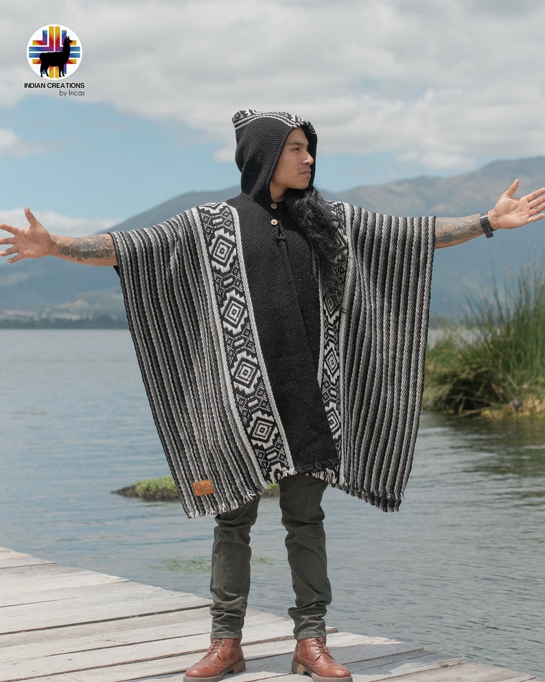 Pode incluir: Um poncho com capuz listrado preto e branco com um padr&atilde;o geom&eacute;trico. O poncho &eacute; feito de l&atilde; de alpaca e tem uma bainha de franjas. O modelo est&aacute; usando o poncho com uma cal&ccedil;a verde escura e botas marrons.