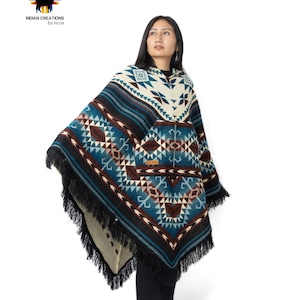 May include: A blue and white hooded poncho with geometric patterns and black fringe. The poncho has a pocket on the front and is made of alpaca wool.